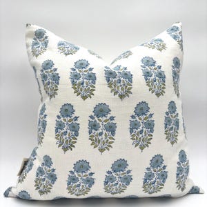 May include: Square decorative pillow with a white background and a repeating pattern of blue floral bouquets with green leaves. The pillow has a soft, textured appearance.