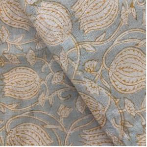 May include: Close-up of a folded fabric with a floral pattern. The fabric has a light blue background with a repeating design of white and gold-colored flowers and vines. The fabric appears to be soft and textured.