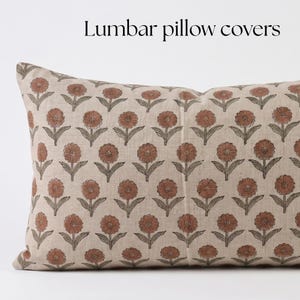 Può includere: Una federa rettangolare per cuscino lombare con un motivo floreale ripetuto di fiori color terracotta con steli e foglie verde scuro su uno sfondo in tessuto beige chiaro. Il testo "Lumbar pillow covers" è stampato sopra il cuscino.