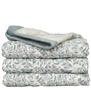 May include: A folded quilt featuring a white base with a repeating sage green floral pattern. The quilt has a solid sage green border along the top edge, showcasing a quilted texture throughout the fabric layers stacked in a neat pile.