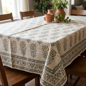 May include: A rectangular tablecloth featuring a cream-colored base with a repeating pattern of muted brown and blue floral motifs. The fabric has a wide decorative border with intricate blue and brown scrolling leaf and vine designs.