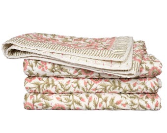 May include: A folded quilted blanket featuring a repeating floral pattern with pink flowers and sage green leaves on a white background. The edges are finished with a striped border in sage green and white, showcasing visible stitching throughout.