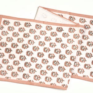 May include: A white table runner with a pink floral pattern. The runner has a pink border.