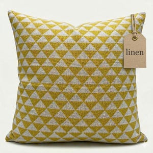 Könnte beinhalten: Quadratisches Leinenkissen mit einem geometrischen Muster aus gelben und grauen Dreiecken. Ein braunes Etikett mit dem Wort "linen" ist angebracht. Ein dekoratives Wohnaccessoire.