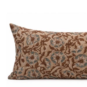May include: A rectangular throw pillow featuring a tan base color with a repeating floral pattern in shades of brown and muted blue. The design consists of stylized flowers and winding vines printed across the entire surface of the fabric.