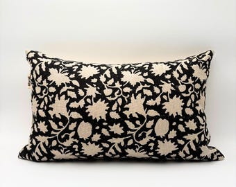 Könnte beinhalten: Rechteckiges Zierkissen mit einem schwarzen und cremefarbenen Blumenmuster. Das Kissen hat ein sich wiederholendes Design aus stilisierten Blumen und Blättern. Der Stoff hat ein strukturiertes Aussehen und ist vor einem weißen Hintergrund platziert.