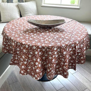May include: Round tablecloth featuring a floral design in brown and white. A decorative metal bowl is placed on top. The tablecloth covers a round table.