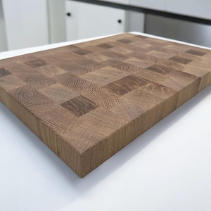 May include: A large, rectangular wooden cutting board with a checkered pattern. The board is made of light and dark wood, creating a contrasting effect. The board is made of solid wood and is designed for durability.