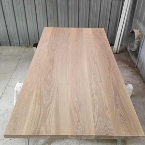 May include: A rectangular wooden table with a light brown finish. The tabletop is supported by four silver metal legs. The wood grain is visible, adding texture to the surface. The table is likely for indoor use.