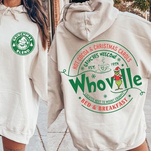 Peut inclure: Un sweat &agrave; capuche blanc avec un logo vert Grinchmas Blend sur le devant et un logo vert Whoville au dos. Le logo Whoville comprend le texte "Hot Cocoa & Christmas Carols", "Grinches Welcome", "Est. 1954", "Located Next to Mount Crumpit", et "Bed & Breakfast".