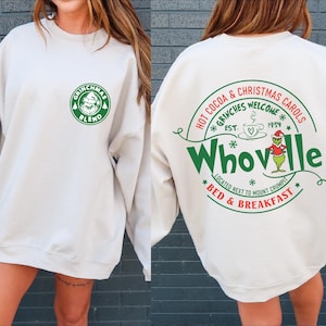 Peut inclure: Un sweat-shirt blanc avec un imprim&eacute; graphique vert et blanc d'un caf&eacute; sur le th&egrave;me du Grinch appel&eacute; "Grinchmas Blend" sur le devant et un imprim&eacute; graphique vert et blanc d'une enseigne sur le th&egrave;me du Grinch qui dit "Hot Cocoa & Christmas Carols *Grinches Welcome* Est. 1954 *Whoville* Located next to Mount Crumpit *Bed & Breakfast*" au dos.