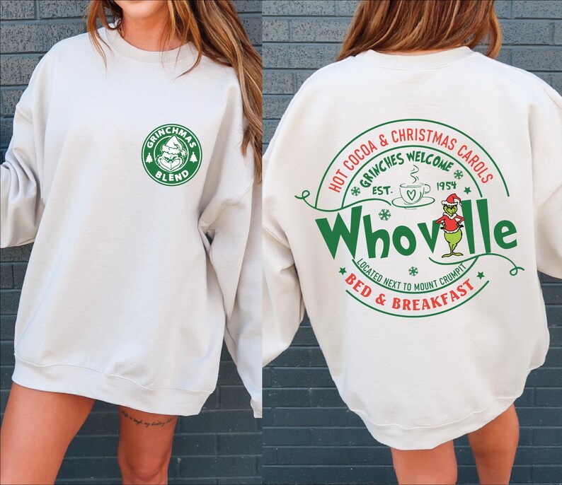 Peut inclure: Un sweat-shirt blanc avec un imprim&eacute; graphique vert et blanc d'un caf&eacute; sur le th&egrave;me du Grinch appel&eacute; "Grinchmas Blend" sur le devant et un imprim&eacute; graphique vert et blanc d'une enseigne sur le th&egrave;me du Grinch qui dit "Hot Cocoa & Christmas Carols *Grinches Welcome* Est. 1954 *Whoville* Located next to Mount Crumpit *Bed & Breakfast*" au dos.