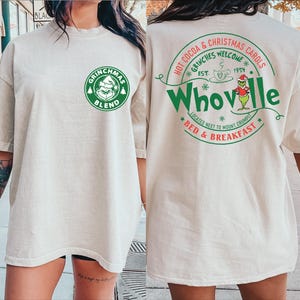 Peut inclure: Un t-shirt blanc avec un logo vert Grinchmas Blend sur le devant et un logo vert Whoville au dos. Le logo Whoville comprend le texte "Hot Cocoa & Christmas Carols", "Grinches Welcome", "Est. 1954", "Located next to Mount Crumpit", et "Bed & Breakfast".