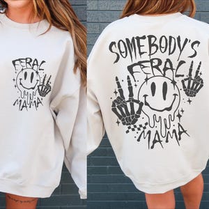 May include: White sweatshirt with black graphic print. The graphic features a smiling face with the text "Somebody's Feral Mama" and skeletal hands.