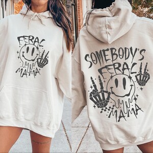 May include: A white hoodie with a black graphic print of a smiley face with dripping eyes and the text "Somebody's Ferac My Mama" on the back. The front of the hoodie has a similar graphic with the text "Ferac My Mama".