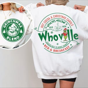 Peut inclure: Sweat-shirt blanc avec un motif Grinchmas vert et rouge. Le devant du sweat-shirt pr&eacute;sente un cercle vert avec les mots "Grinchmas Blend" et un dessin anim&eacute; du Grinch. Le dos du sweat-shirt pr&eacute;sente un cercle vert avec les mots "Hot Cocoa & Christmas Carols *Grinches Welcome* Est. 1954 Whoville *Located Next to Mount Crumpit* Bed & Breakfast*"