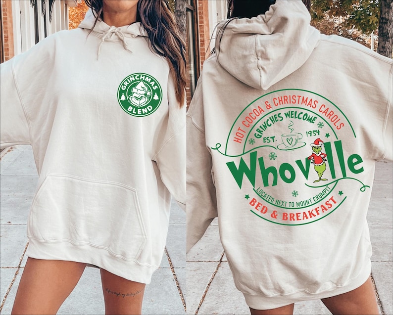 Peut inclure: Un sweat &agrave; capuche blanc avec un logo vert Grinchmas Blend sur le devant et un logo vert Whoville au dos. Le logo Whoville comprend le texte "Hot Cocoa & Christmas Carols", "Grinches Welcome", "Est. 1954", "Located Next to Mount Crumpit", et "Bed & Breakfast".
