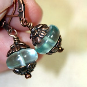May include: A pair of earrings with a light blue glass bead and a copper filigree design.