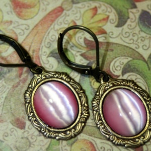 May include: A pair of gold tone earrings with pink and white cat's eye stones set in ornate frames.