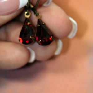 May include: A pair of dangle earrings with red teardrop-shaped crystals and gold-toned metal.