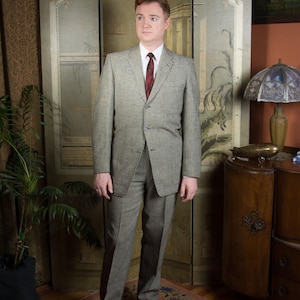 Peut inclure: Un costume gris clair avec une chemise blanche et une cravate bordeaux. Le costume a une coupe classique et ajustée. La personne se tient sur un tapis à motifs devant un paravent décoratif.