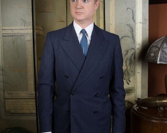 May include: A navy blue double-breasted suit with a subtle pinstripe pattern. The suit features a white dress shirt and a blue tie. The trousers are gray. The suit is a classic style, suitable for formal occasions.