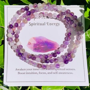 May include: Three amethyst beaded bracelets are displayed on a white card with the words "Spiritual Energy." The card also features a purple crystal illustration and text that reads "Awaken your inner vision... Boost intuition, focus, and self-awareness."