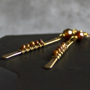 Puede incluir: Un par de pendientes largos de oro con cuentas marrones y una piedra marrón más grande en la parte superior.