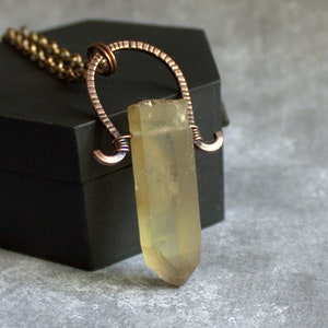 May include: A yellow crystal pendant necklace with a copper wire wrapped around it. The pendant is hanging from a copper chain.