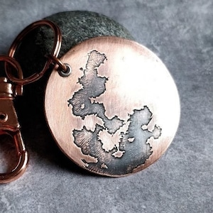 May include: A copper keychain with a round charm featuring a detailed etched design of an island. The keychain has a silver-toned clasp.