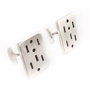 May include: A pair of silver cufflinks with a geometric pattern. The cufflinks are square shaped with a brushed silver finish.
