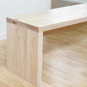 May include: A light wood bench with a simple design. The bench is made of solid wood and has a natural finish.