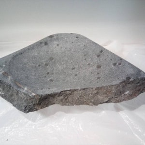 May include: A gray stone bowl with a rough, uneven surface. The bowl is shaped like a shallow dish with a wide, rounded rim.