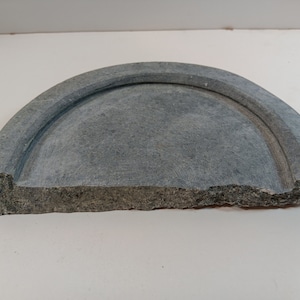 May include: A gray stone half-circle dish with a raised rim. The dish is slightly chipped on the edge.