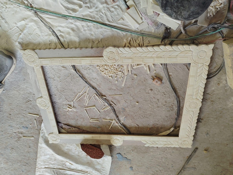 May include: A rectangular, light-colored wooden picture frame featuring intricate carved floral motifs at each corner and a repeating leaf pattern along the inner border, showcasing detailed craftsmanship and a natural, unfinished wood texture.