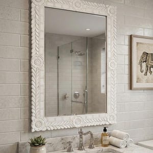 May include: A rectangular wall mirror featuring a white frame with intricate carved floral and leaf patterns. The frame has circular motifs at each corner and along the sides, providing a textured, detailed border around the reflective glass surface.