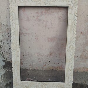 May include: A rectangular mirror frame featuring an off-white, cream-colored finish with intricate hand-carved floral motifs at each corner and center point, complemented by a repeating leaf-like pattern along the entire border edge.