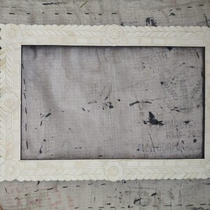 May include: A rectangular off-white picture frame featuring intricate carved leaf patterns along the borders and circular floral motifs at each corner and the center of every side, creating a detailed and symmetrical decorative border.