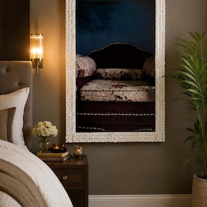 May include: A rectangular wall mirror featuring a thick, white, hand-carved frame with intricate leaf-like patterns along the edges and circular floral motifs at the center of each side, reflecting a dark room with a patterned armchair.