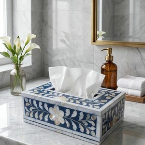 Op de afbeelding: Decoratieve tissuebox met een blauw en wit bloemmotief. De doos is rechthoekig en heeft een parelmoer inlegwerk met een bloemmotief. Witte tissues zijn zichtbaar. De doos staat op een marmeren aanrecht.