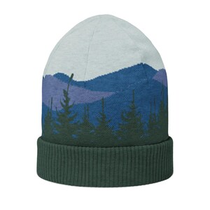 Op de afbeelding: Een gebreide beanie met een berg- en bosontwerp. Het heeft een donkergroene geribbelde manchet en een lichtblauwe kroon. Het ontwerp bevat blauwe en paarse bergen en donkergroene bomen.
