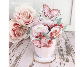 May include: A pink teacup with a saucer and a bouquet of pink and red flowers with two butterflies. The flowers are made of paper and the teacup is a 3D pop-up card.