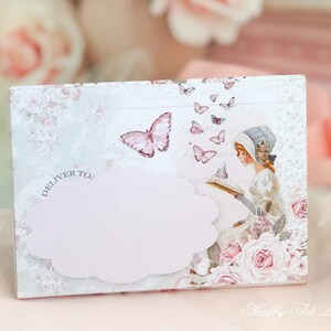 May include: A white card with a pink cloud and the text "Deliver To:" printed on it. The card has a floral design with butterflies and a girl reading a book.