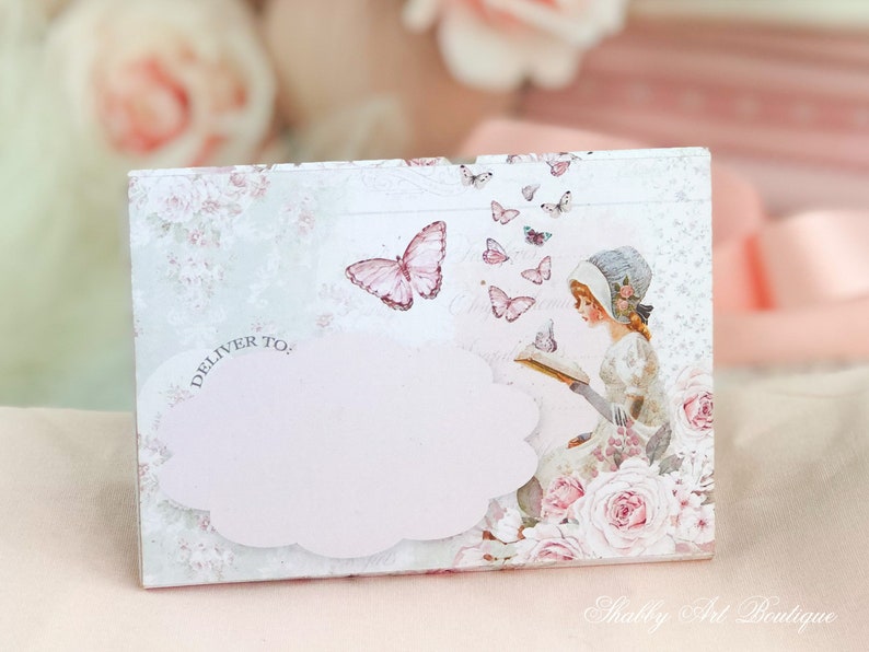 May include: A white card with a pink cloud and the text "Deliver To:" printed on it. The card has a floral design with butterflies and a girl reading a book.