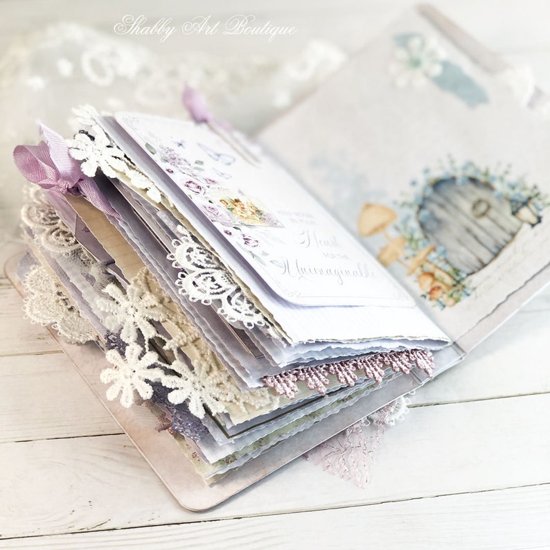May include: A white and purple journal with lace trim and a floral design. The journal is open to reveal a page with the text "Heart & Home" written in cursive.