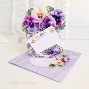 Peut inclure: Une carte pop-up florale violette et jaune avec une tasse &agrave; th&eacute; et une soucoupe. La carte a une carte postale attach&eacute;e avec un clip.