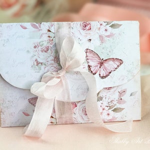 May include: A white envelope with a floral design and a pink butterfly. The envelope is tied with a white ribbon and has the text "Shabby Art Boutique" printed on the bottom.