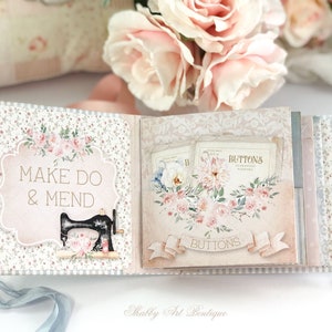 May include: A small, pink and white scrapbook with a floral design. The cover has the text "Make Do & Mend" and a black sewing machine illustration. The inside pages feature a floral design with the text "Buttons".