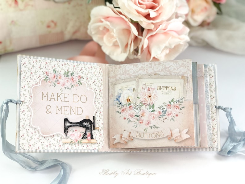 May include: A small, pink and white scrapbook with a floral design. The cover has the text "Make Do & Mend" and a black sewing machine illustration. The inside pages feature a floral design with the text "Buttons".