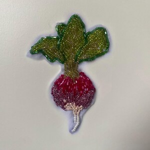 May include: A beaded radish with green leaves and a white stem. The radish is pink and purple.